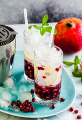 refreshing alcoholic drink with lemon and pomegranate seeds on a white stone table and gray background with mint and bar accessories