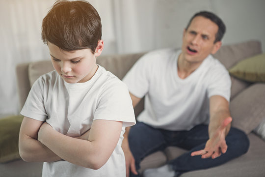 Do not be so naughty. Annoyed man is screaming at his upset son. Focus on depressed boy