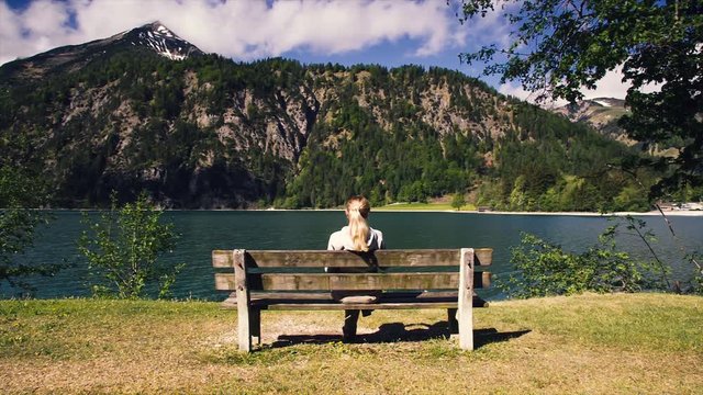Mountain view the girl sits on a bench and enjoys the view. Alone girl on chair see view sightseeing  mountain lake views. Girl relaxing on cosy romantic bench in mountains by lake norway, austria.