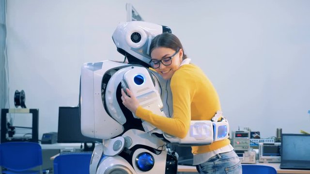 Young woman is coming to a human-like robot, they are hugging and talking
