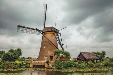 Fototapeta na wymiar Windmill with house and garden on the bank of a large canal in a cloudy day at Kinderdijk. Situated in a polder, has the largest concentration of old windmills in the country. Southern Netherlands.