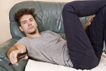 Fototapeta premium A young man watches television and changes channels while relaxing