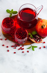 freshly prepared pomegranate juice in a decanter and two glasses on a marble table and a gray stone background with mint leaves and fruit seeds