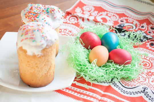 Easter cakes on a plate and the bright colored Easter eggs. Painted chicken eggs are in artificial decorative straw. Festive symbol on the table.