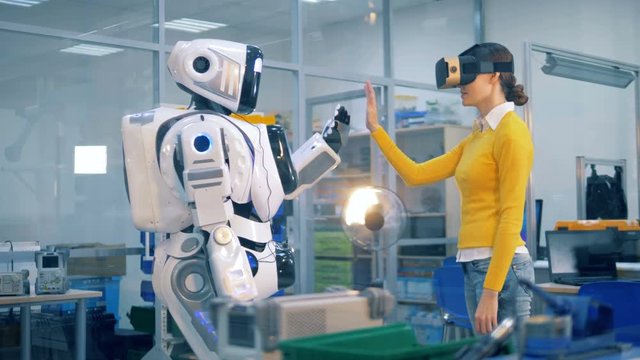 Robotic humanoid is doing a high-five to a lady in virtual reality glasses