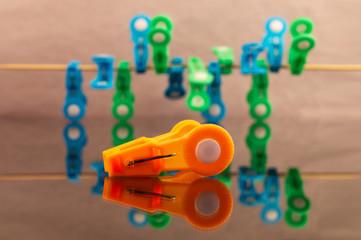 Orange clothespin close-up against a background of blue and green clothespins fixed on a stretched rope with reflection in the glass.