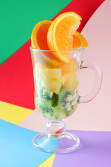 Pieces of tropical fruits in a glass, fruit cocktail. Sliced orange, kiwi cubes, slices of pineapple in a glass bowl. Multi-colored pop art background