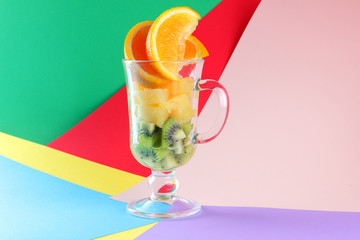 Pieces of tropical fruits in a glass, fruit cocktail. Sliced orange, kiwi cubes, slices of pineapple in a glass bowl. Multi-colored pop art background