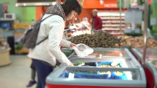 A young woman chooses a green frozen string bean in a self-service store. A girl is buying vegetables in a supermarket.