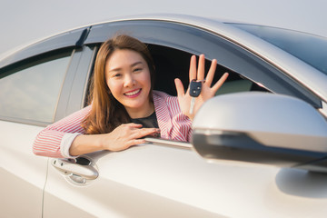 Asian driver woman smiling and showing new car key while sitting in a car that she taking it from dealer in the auto show. transport business, car sale for consumerism and people concept,vintage color