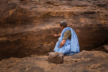 Beduin pointing to rock structure with ancient engravings in the Sahara