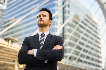 Confident, smiling man outdoors,Young businessman thoughtful wearing suit holding hand arms, looking out of modern office, planning future project, Business Concept.