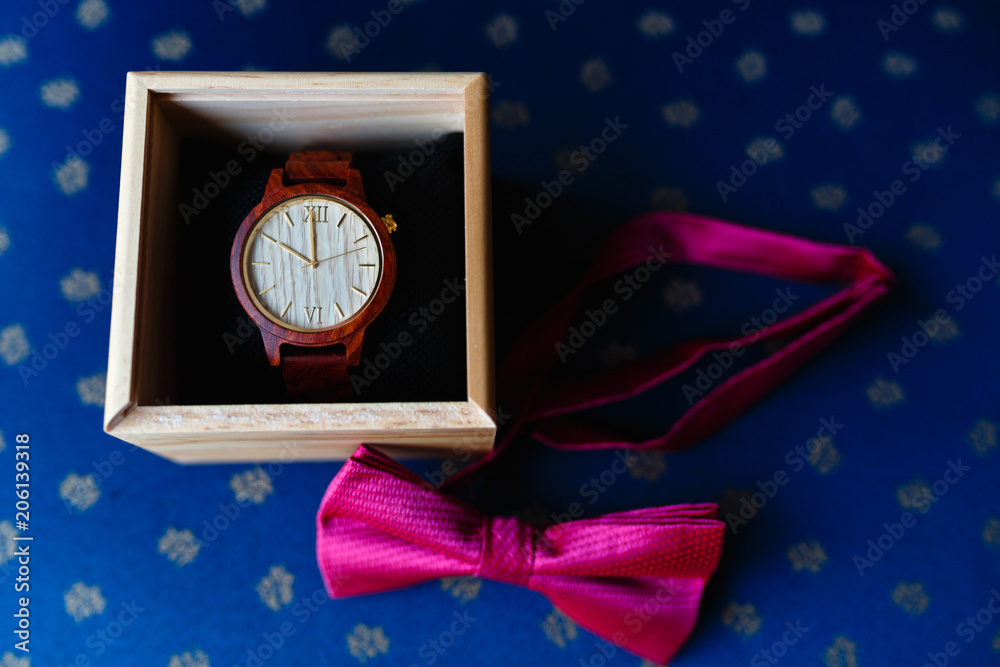 Wall mural stylish wristwatch in a wooden box. pink bow tie. a men's set of accessories on an old wooden chair 