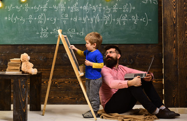 Teacher checks student writing on chalkboard. Pupil talking to his tutor or daddy while solving the...
