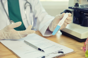 female Doctor hands with positive pregnancy test for a pregnant girl at doctor's office,Medical report and enceinte, gravid urine test strips,The doctors are wearing a white coat.