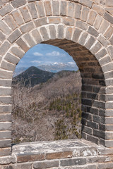 Beijing, China - April 28, 2010: Great Wall of China at Badaling. Window in the wall shows gray-green wilderness and mountains with snow tops on horizon under blue sky.