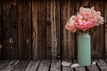 A bunch of pink peonies in a green vase on the right side of a rustic plank table leaving room for copy.