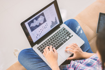 Beautiful young Asian woman working with laptop in living room, making notes in documents file on computer,Analyze financial report for business plan, small business concept,morning light,vintage tone