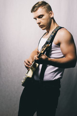 Musician playing music. Modern style guitar player. Man with electric guitar. Portrait of adult musician playing instrument. Young muscular man in casual clothes playing guitar on gray background.