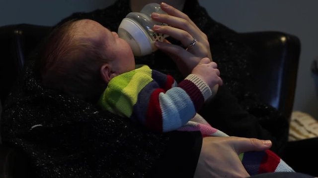 newborn baby is bottle fed milk in mothers loving arms