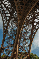 View of one leg’s iron structure of the Eiffel Tower, with blue sky and sunshine in Paris. Known as the “City of Light”, is one of the most impressive world’s cultural center. Northern France.