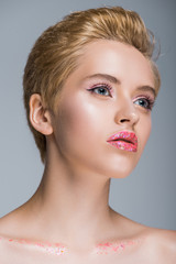 low angle view of attractive woman with glitter on lips and body looking away isolated on grey