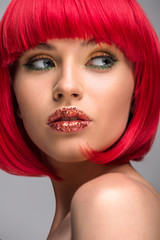 Naklejka premium portrait of beautiful woman with red hair and glitter on face looking away isolated on grey