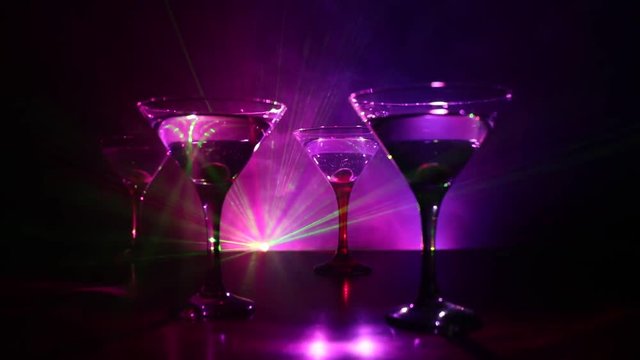 Alcohol drink poured into martini glasses of bottle. Several glasses of famous cocktail Martini, shot at a bar with dark toned foggy background and disco lights. Club drink concept
