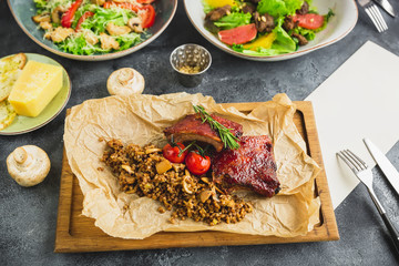 Barbecued spare ribs meat, buckwheat with mushroom and tomatoes on wooden cutting board and salats. Paper menu.