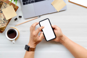 Man using mobile phone on office white wooden desk table with computer , office supplies and coffee cup.