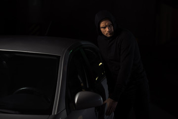 focused male thief in black hoodie intruding automobile