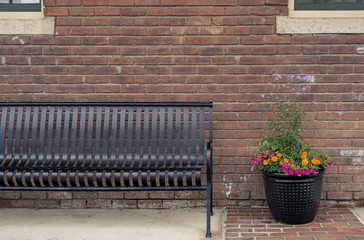 Community City Park bench on sidewalk or pathway beside decorative planter ready for someone to sit and enjoy a minute of rest or conversation
