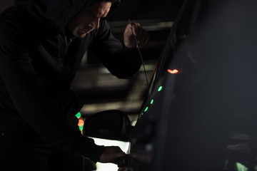 male thief in black hoodie intruding car by picklock