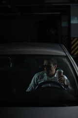 male undercover agent in sunglasses sitting in car with paper cup of coffee