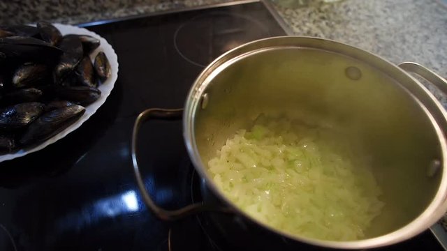 Close-up of an onion being fried in a pan. Steam above the pot. Preparation of white sauce for mussels.