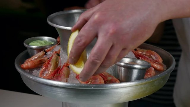 The cook prepares dish of boiled shrimp on ice with lemon and sauces in the restaurant's kitchen. Recipes for cooking. Slow motion shot.
