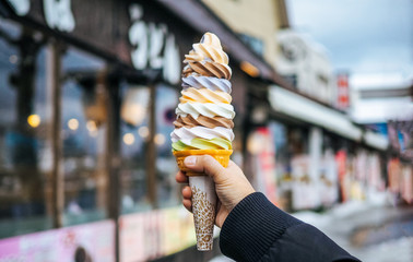A women hand holding mixed colorful tasty ice cream soft cream cone with blurred shop background (selective focus)