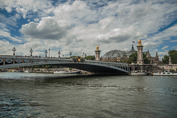 Fototapeta na wymiar Alexandre III bridge, Grand Palais building and boats anchored at Seine River bank in Paris. Known as the “City of Light”, is one of the most impressive world’s cultural center. Northern France.