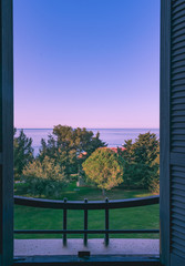 Beautiful sunrise viewed from an open window with blue wooden shutters, view of the Adriatic sea and a Mediterranean style house in Croatia