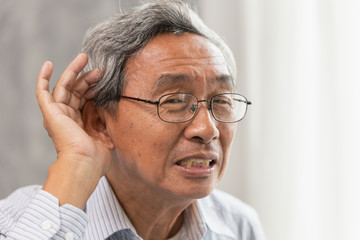 Obraz premium Asian old man with Deaf Hearing problems place hand on ear for help listening louder.