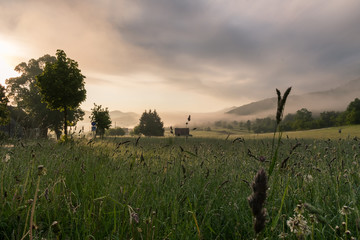 Misty mountains, early hazy morning over a mountain meadow or a field with green forested hills, Krasno polje village near Velebit mountain national park in Croatia