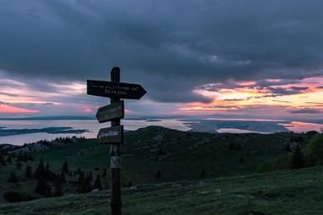 View of a signpost for mountaineers on the Velebit mountain in Croatia with islands and the Adriatic sea in the background during a colorful sunset.