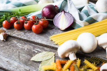 Fresh ingredients for cooking pasta, tomato and spices over wooden table background with copy space