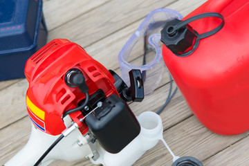 filling up with fuel from a red canister with gasoline, manual lawn mower close-up, on a wooden...