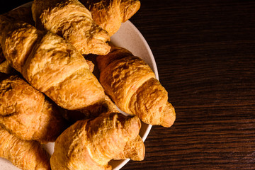 Plate with fresh croissants on a dark wooden table. Top view