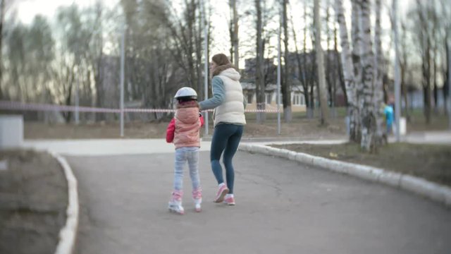 Mom and daughter ride on roller skates. Girl learning to roller skate, and falls. Mom teaches daughter to ride on rollers