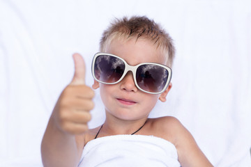 A little kid lies on a white blanket in white glasses and is happy