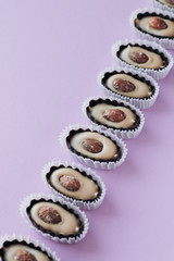 Flat lay of delicious praline sweets with almonds on purple background