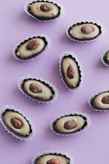 Flat lay of delicious praline sweets with almonds on purple background