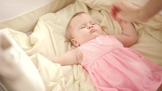 Beautiful baby sleeping in crib. Mother hands stroking sleeping kid. Child girl in pink dress sleeping in cot. Toddler rest in bed. Mother care. Baby bedtime